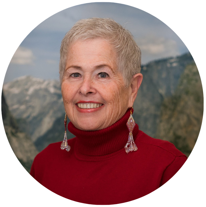 Woman with long earrings smiling at camera in front of a mountain