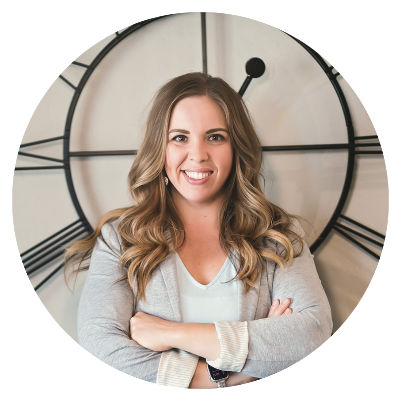 Woman with long hair and arms folded standing in front of a large clock